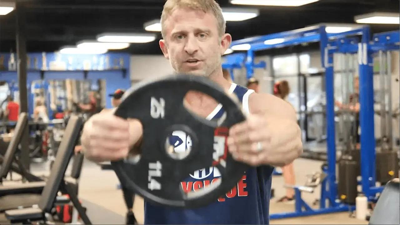 Plate front raise demonstrating the grip variation for front delt isolation